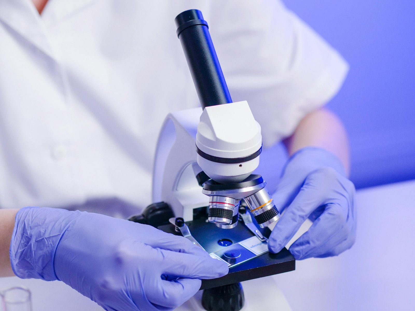 Scientist wearing gloves preparing a slide on a laboratory microscope for research analysis.